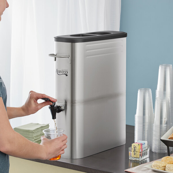 A person using an Avantco 5 Gallon Slim Iced Tea Dispenser to pour a drink into a glass.