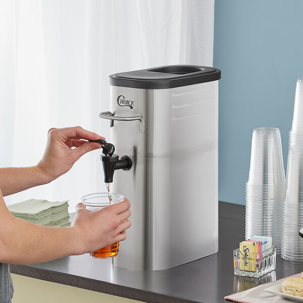A woman pouring iced tea from a Choice Slim Iced Tea Dispenser into a glass.
