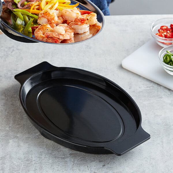 A person using a black oval Choice bakelite underliner with handles to carry a plate of shrimp and vegetables.