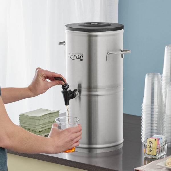 A person pouring a drink from an Avantco stainless steel iced tea dispenser.