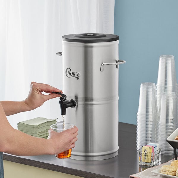A woman pouring iced tea from a Choice stainless steel iced tea dispenser into a glass.