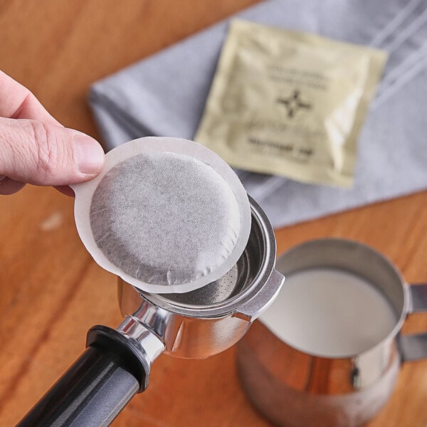 A hand using a Caffe Verani double-shot espresso pod in a silver holder over a coffee machine.