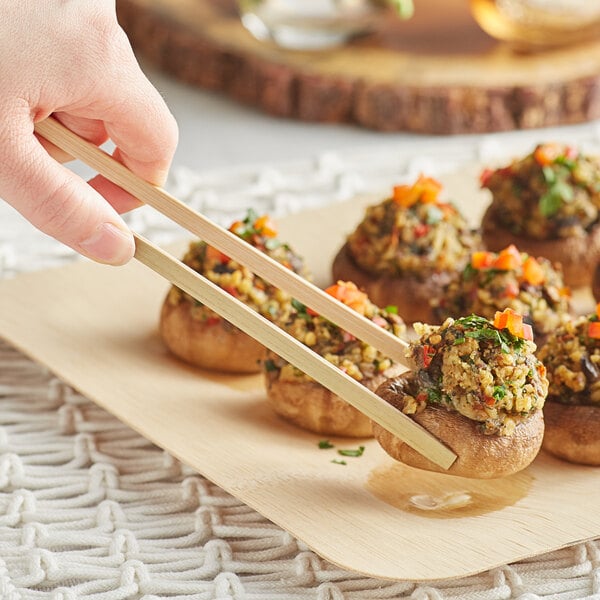 A person using Bamboo by EcoChoice tongs to serve mushrooms on a plate.
