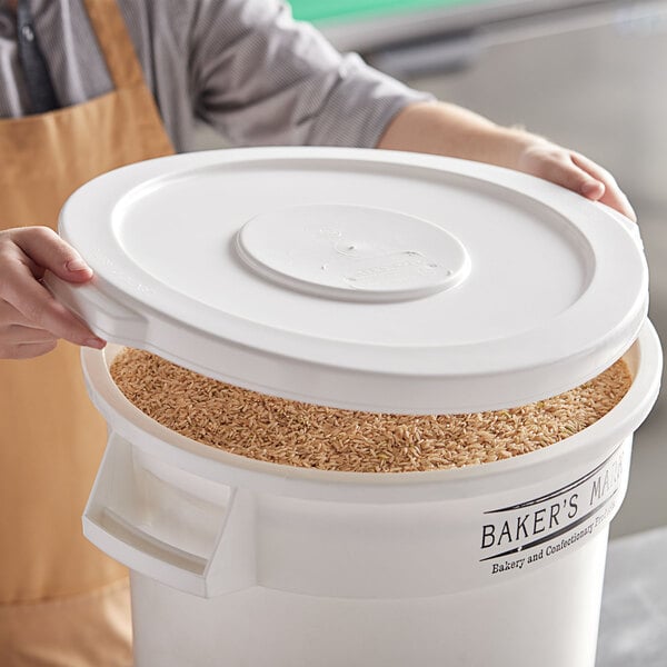 A person holding a Baker's Mark white ingredient bin lid filled with brown rice.