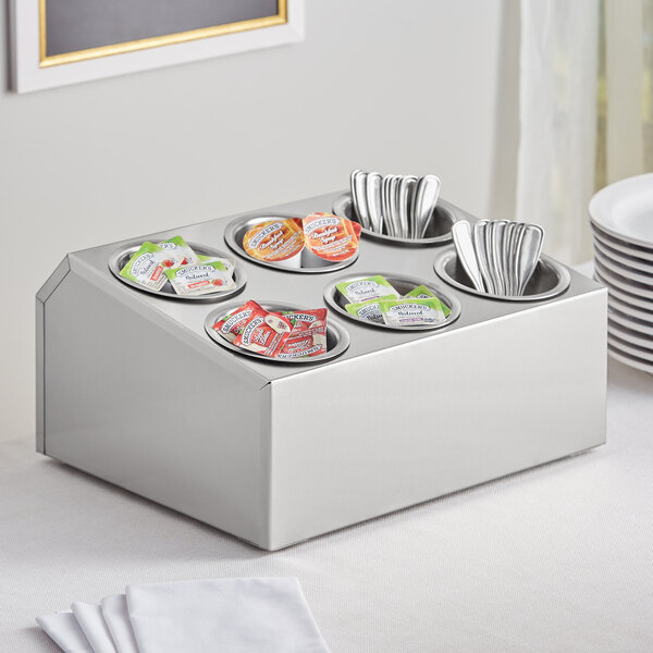 A stainless steel flatware organizer with six cylindrical cups holding silverware and utensils.