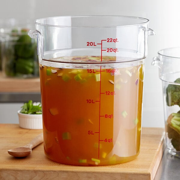 A Cambro clear round polycarbonate food storage container filled with liquid on a counter.