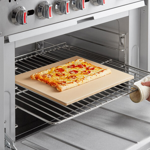 A rectangular pizza stone with a pizza being placed in an oven.