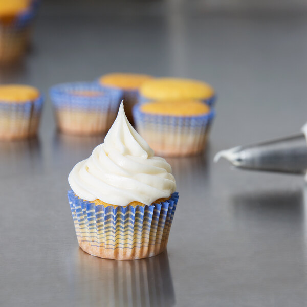 A cupcake with white frosting in a blue and white striped baking cup.