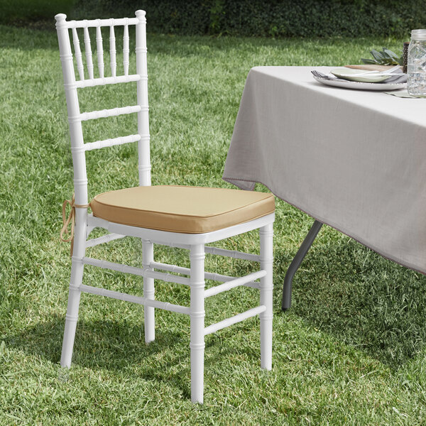 A white Lancaster Table & Seating Chiavari chair with a tan cushion next to a table.