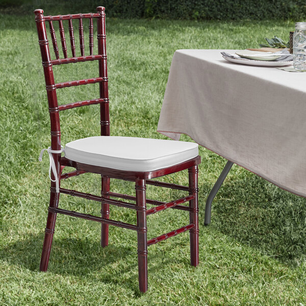 A Lancaster Table & Seating mahogany Chiavari chair with a white cushion next to a table with a white tablecloth.