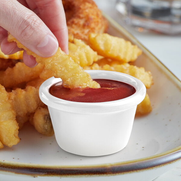 A person dipping a french fry into a white Acopa melamine ramekin filled with red sauce.