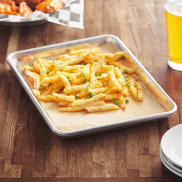 A Baker's Mark aluminum sheet pan with french fries and a glass of beer on a table.