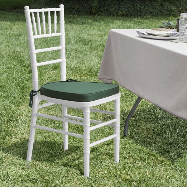 A white Lancaster Table & Seating Chiavari chair with a green cushion next to a table.