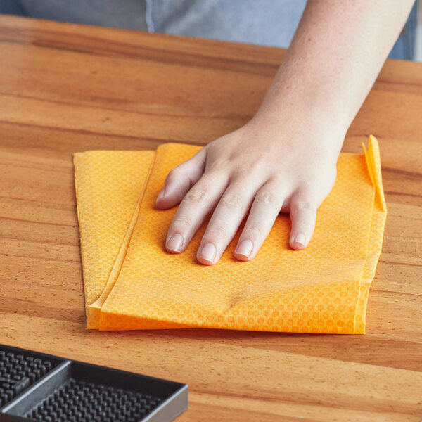 A person using a Lavex orange dusting cloth to clean a wooden table.