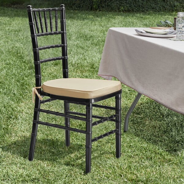 A Lancaster Table & Seating black wood Chiavari chair with a gold cushion on a grassy field.