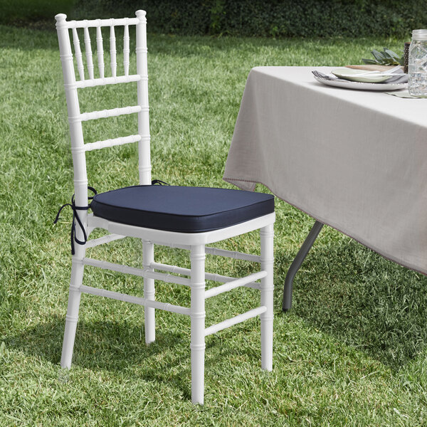 A Lancaster Table & Seating white wood Chiavari chair with a navy blue cushion on it next to a table.