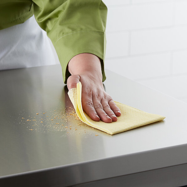 A hand holding a yellow ChoiceHD medium-duty foodservice wiper cleaning a counter.
