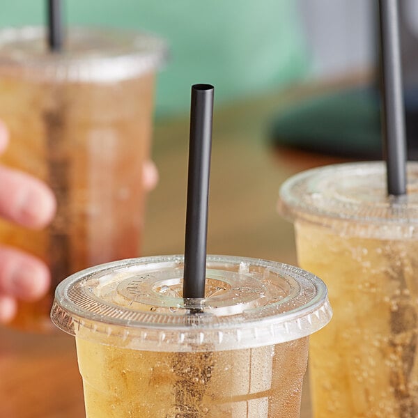 A group of plastic cups with Choice giant black unwrapped straws on a table.