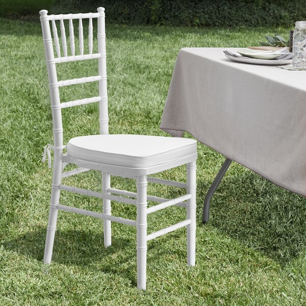 A white Lancaster Table & Seating Chiavari chair with white cushion sits in the grass.