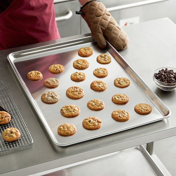A person wearing gloves holding a Baker's Mark wire in rim aluminum sheet pan of cookies.