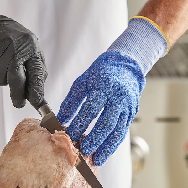 A person wearing blue Mercer Culinary Millennia Fit cut-resistant gloves cutting meat on a butcher shop counter.