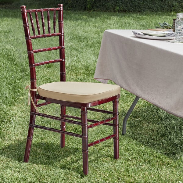 A Lancaster Table & Seating mahogany Chiavari chair with a gold cushion next to a table