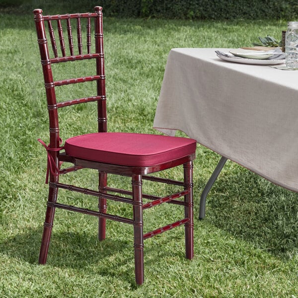 A Lancaster Table & Seating mahogany Chiavari chair with a wine red cushion on a table.