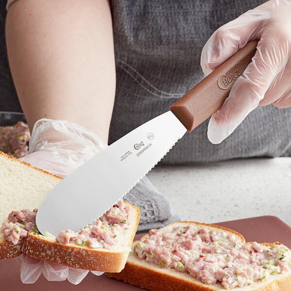 A person using a Choice scalloped sandwich spreader to spread food on a piece of bread.