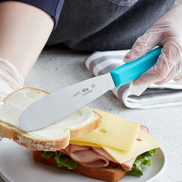 A person using a Choice scalloped sandwich spreader to spread butter on a sandwich.