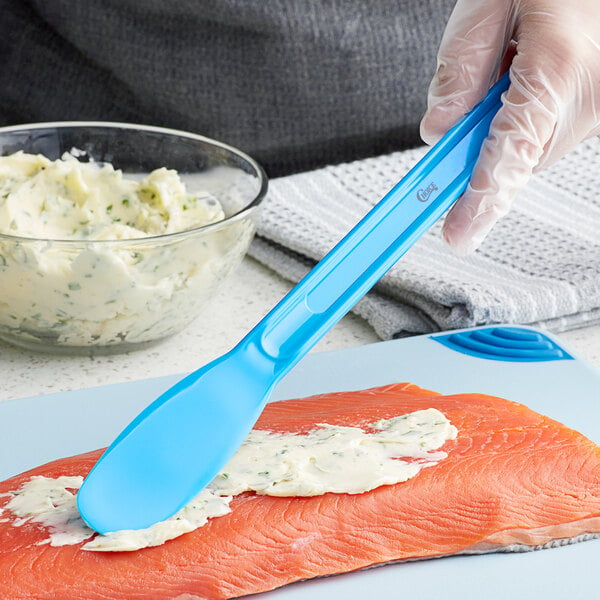 A person's hand with a Choice sandwich spreader spreading white cream on a piece of fish.