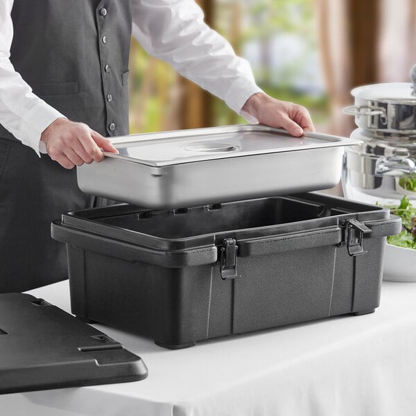 A man in a black apron opening a CaterGator black top loading food pan carrier to reveal a Vigor stainless steel food pan.