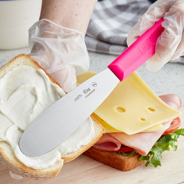 A person spreading a sandwich with a Choice stainless steel sandwich spreader with a neon pink handle.