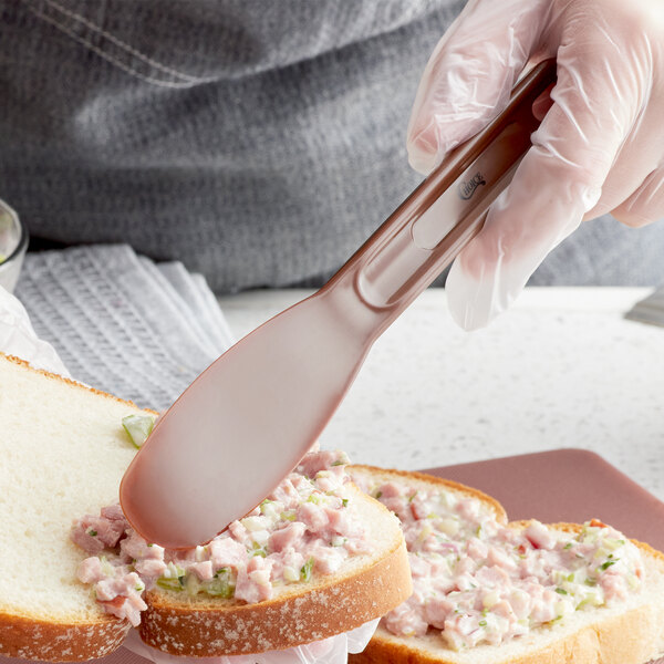 A person holding a Choice brown polypropylene sandwich spreader while spreading food on a sandwich.