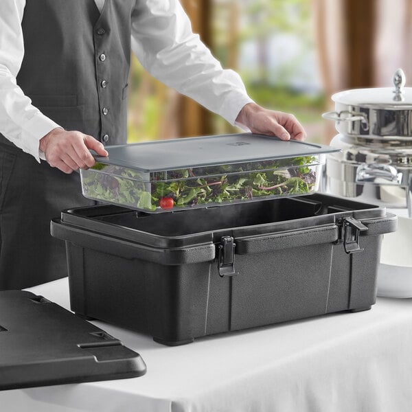 A man using a CaterGator black plastic food pan carrier to hold a container of food on a table.
