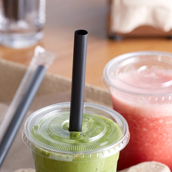 A green smoothie in a plastic cup with a black straw on a table.