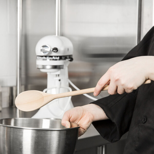 A person in a chef's uniform using a Tablecraft beechwood wooden spoon to stir a bowl.