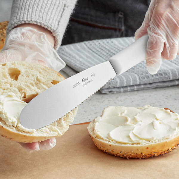 A person using a Choice scalloped sandwich spreader to spread butter on a bagel.