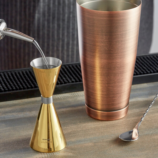 A gold-plated Barfly slim style jigger on a table.