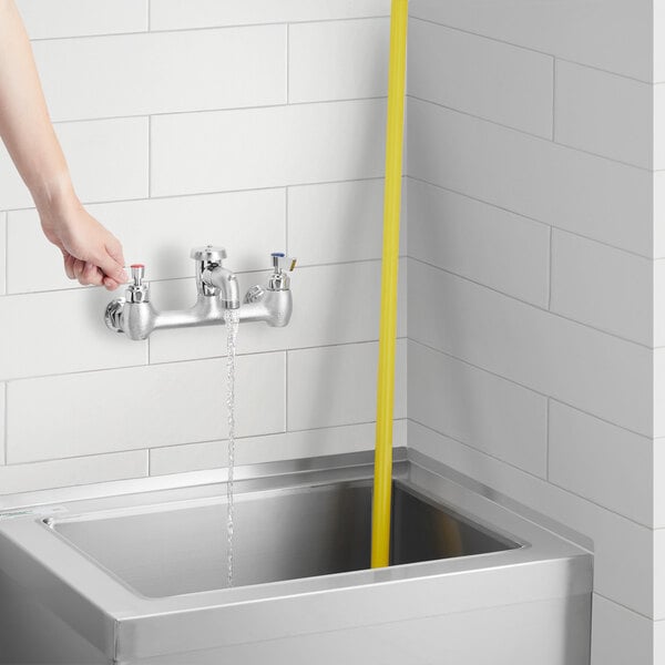 A person using a Waterloo wall-mounted service sink faucet to wash a sink with a yellow hose.