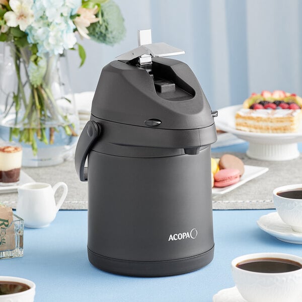 A black Acopa stainless steel coffee airpot on a table with cups of coffee and desserts.