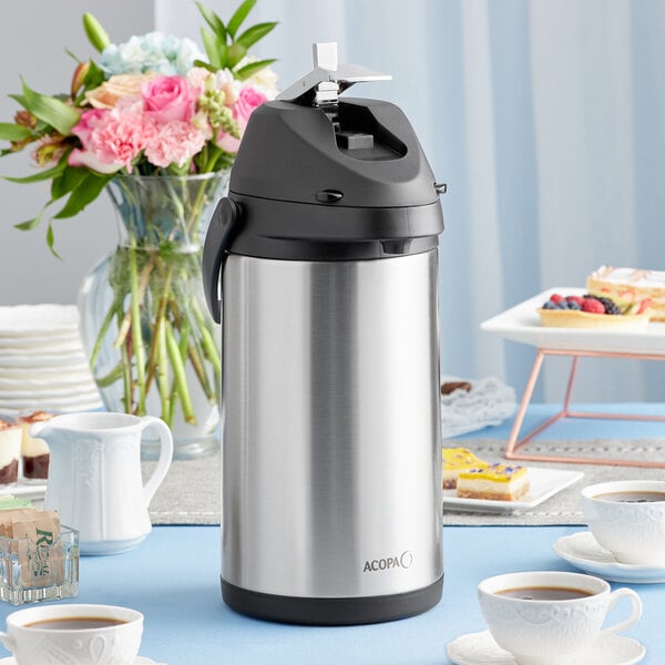 An Acopa stainless steel airpot filled with coffee on a table.