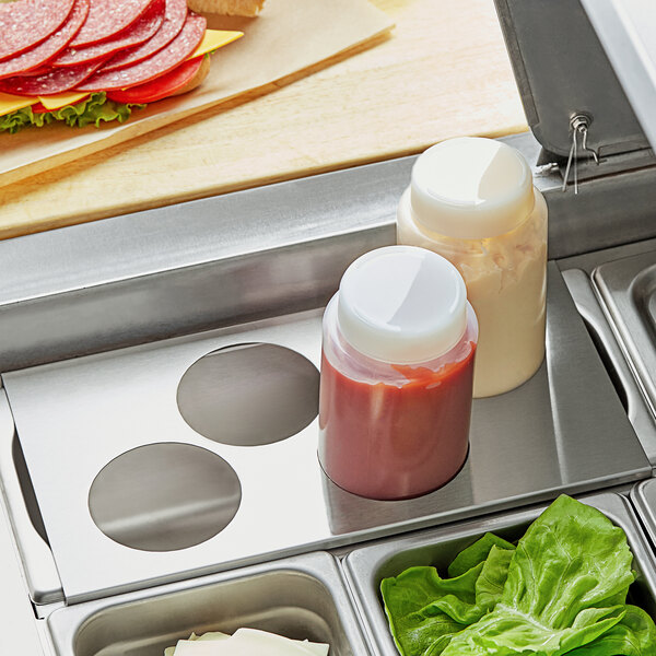 A stainless steel tray with 4 squeeze bottles of condiments on a table.