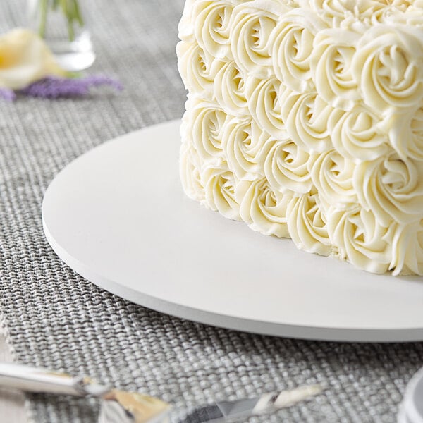 A white cake on an 18" white circular melamine-coated wood cake board with feet.