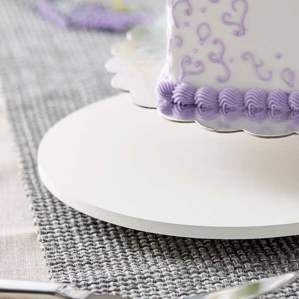 A close-up of a white cake on a 14" circular white wood cake board with feet.
