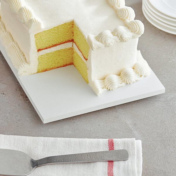 A slice of frosted cake on a white rectangular melamine-coated wood cake board with feet.