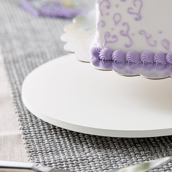 A white circular melamine-coated wood cake board with a cake on it.