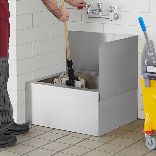 A man using a mop to clean a Regency stainless steel mop sink.