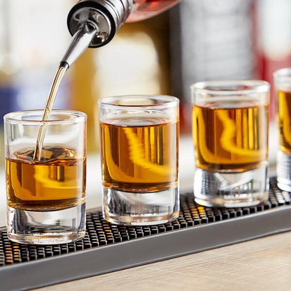 A bartender pouring brown liquid into Pasabahce shot glasses on a bar.