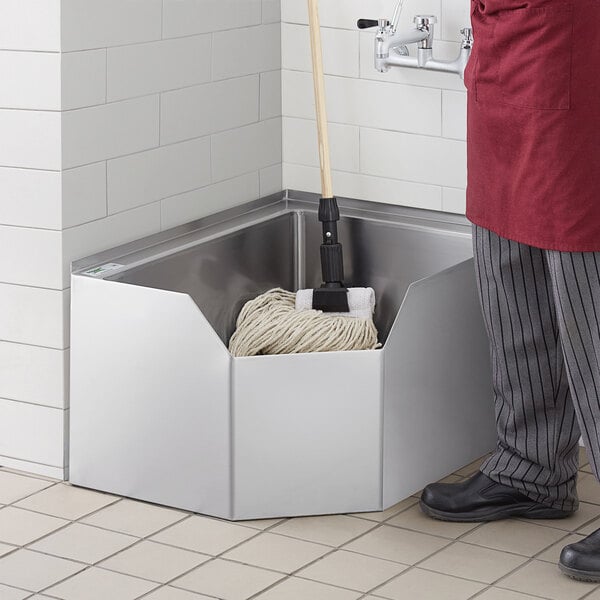 A man in a red apron cleaning a Regency stainless steel corner mop sink.