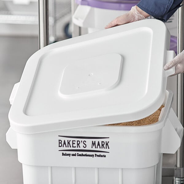 A person wearing gloves putting a white plastic lid on a Baker's Mark white plastic container.